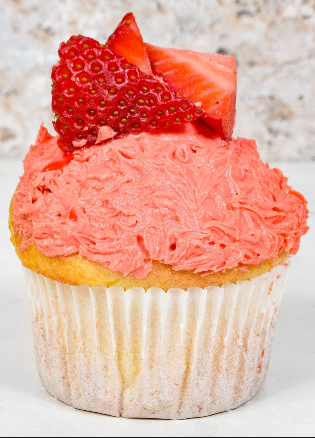 Cupcake with pink frosting and sliced strawberries on a textured surface